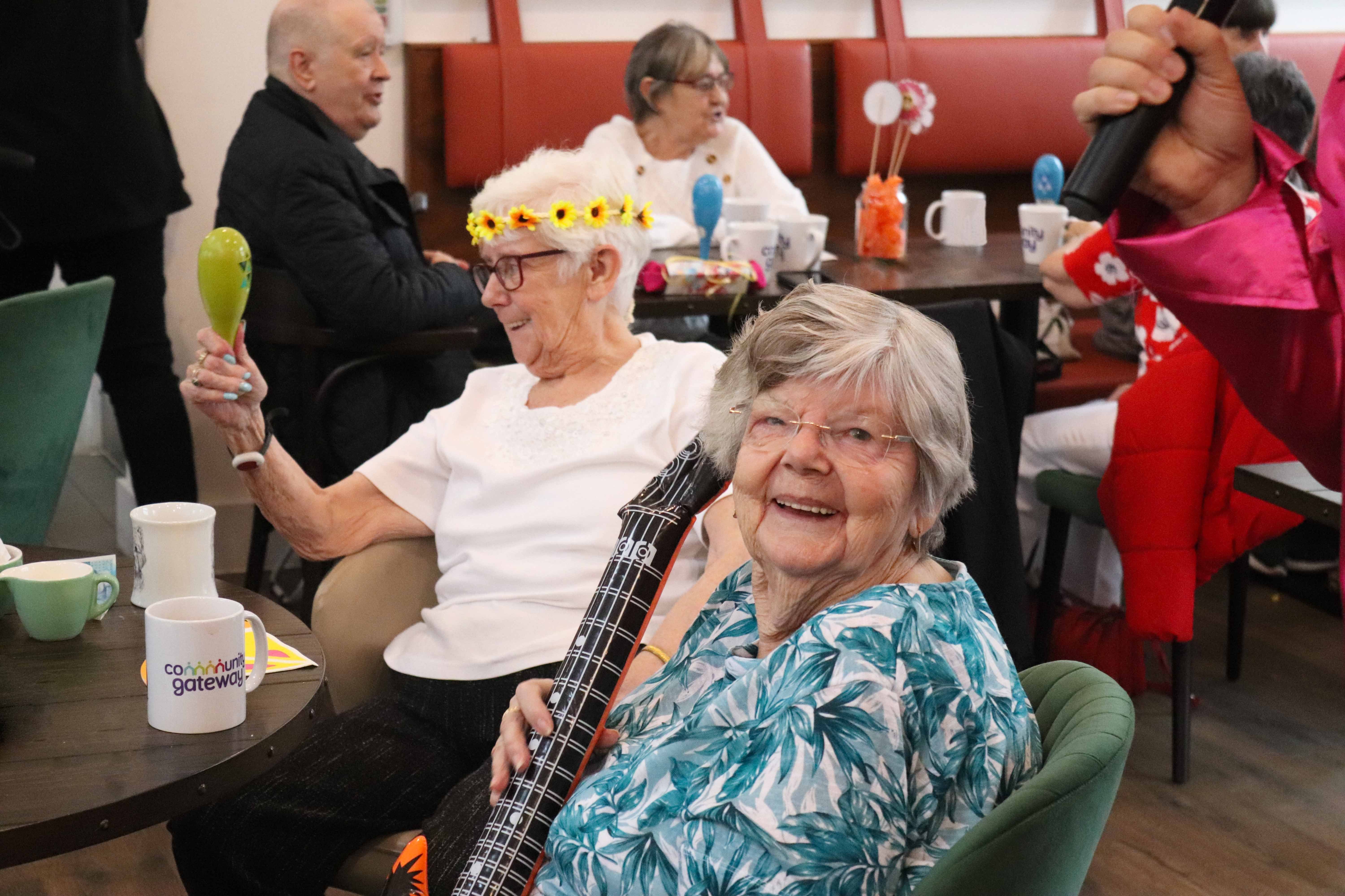 A female woman with grey hair smiling at the camera with an inflatable guitar in her hands